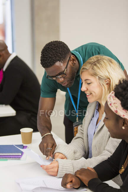 Community college instructor helping students with paperwork in classroom — Stock Photo