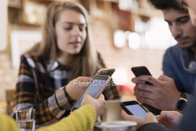 Amigos adultos jóvenes usando teléfonos inteligentes en la cafetería - foto de stock