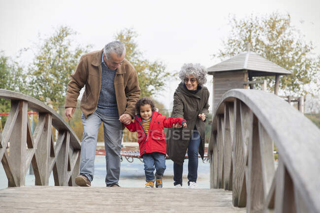 Бабушка с дедушкой идут с внуком по пешеходному мосту — стоковое фото