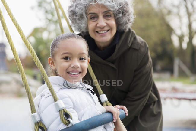 Retrato sorrindo avó e neta brincando no balanço no parque infantil — Fotografia de Stock