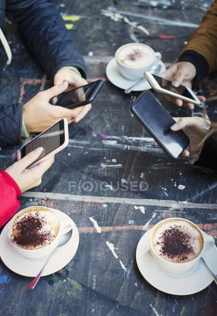 College students using smart phones and drinking cappuccinos at cafe table — Stock Photo