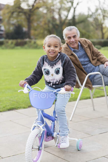 Portrait smiling granddaughter on bicycle with grandfather at park — Stock Photo