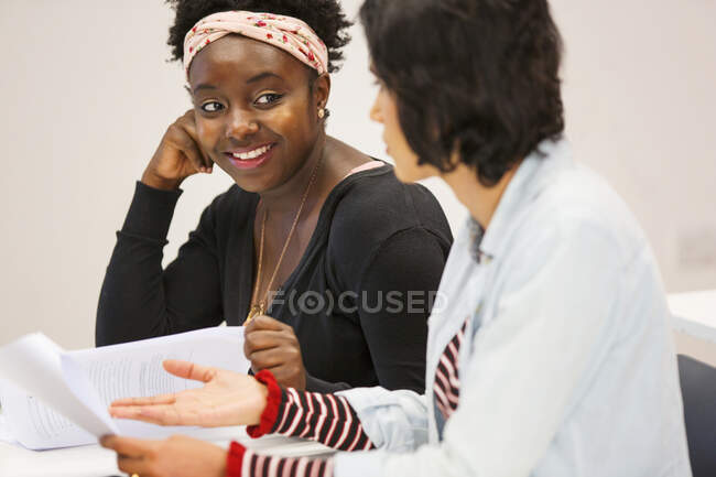 Smiling female community college students talking, discussing paperwork in classroom — Stock Photo