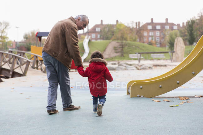 Grand-père marchant avec petit-fils tout-petit à l'aire de jeux — Photo de stock