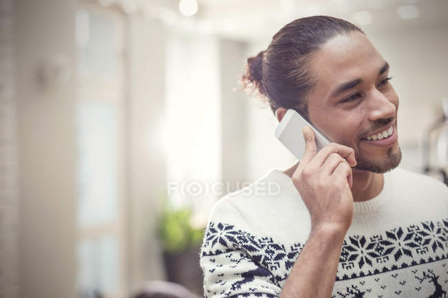 Jeune homme souriant en pull de Noël parlant sur téléphone intelligent — Photo de stock
