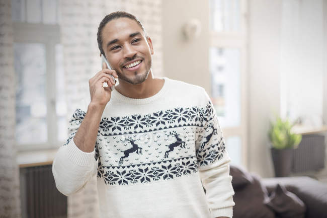 Улыбающийся молодой человек в рождественском свитере разговаривает по телефону — стоковое фото