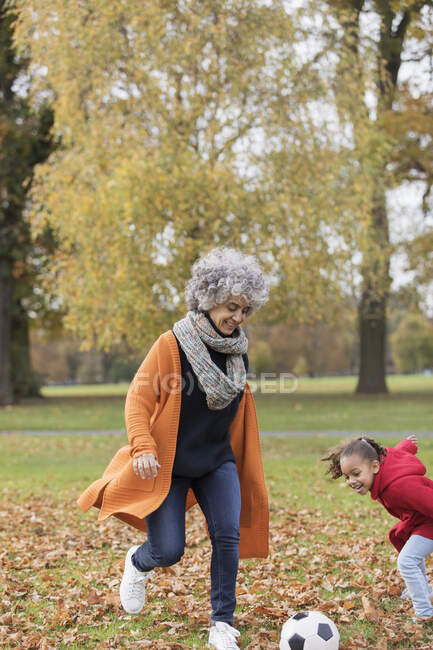 Playful grandmother playing soccer with granddaughter in autumn park — Stock Photo
