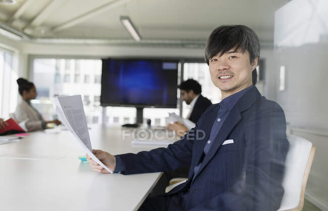 Retrato hombre de negocios confiado revisando el papeleo en la reunión de la sala de conferencias - foto de stock