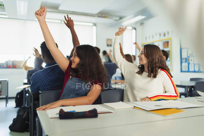 Estudiantes de secundaria con las manos levantadas durante la lección en el aula - foto de stock