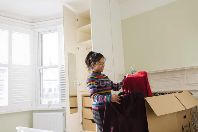 Mulher desembalando roupas de caixa móvel no quarto — Fotografia de Stock