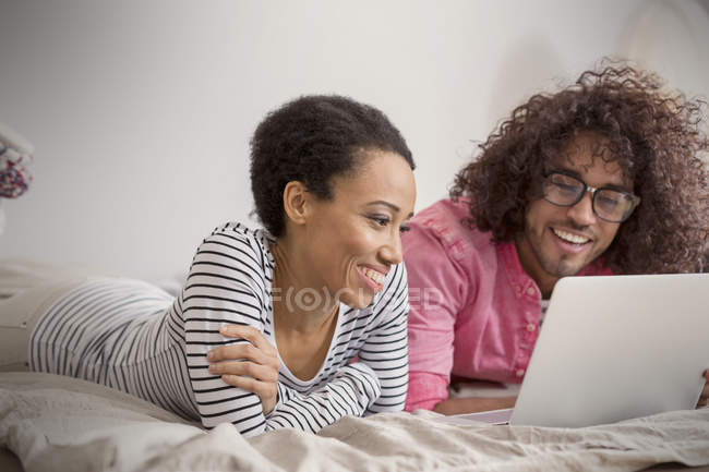 Couple souriant utilisant un ordinateur portable sur le lit — Photo de stock