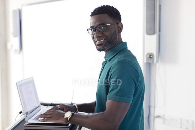 Porträt lächelt, selbstbewusster männlicher Lehrer am Laptop bereitet sich im Klassenzimmer vor — Stockfoto