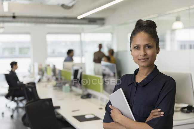 Retrato mujer de negocios con confianza con tableta digital en la oficina de planta abierta - foto de stock