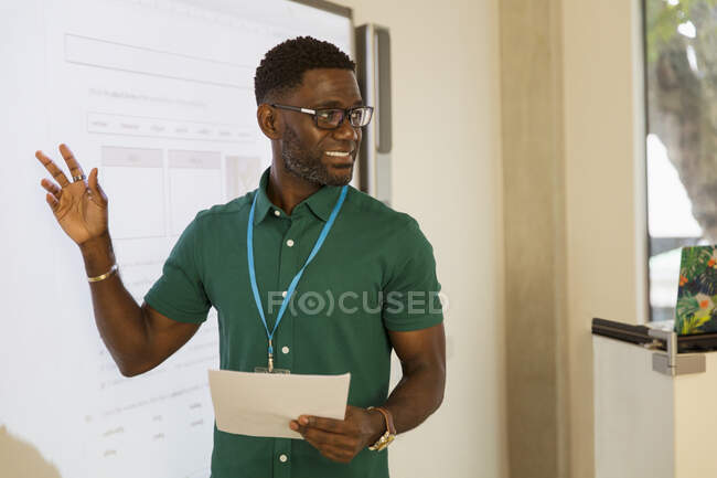 Instructor de universidad comunitaria masculino en la pantalla de proyección en el aula - foto de stock