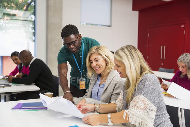 Community college instructor and students discussing paperwork in classroom — Stock Photo