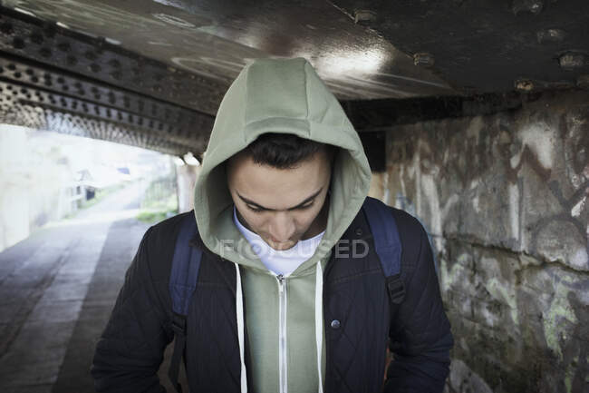 Jeune homme à capuche marchant sous un pont urbain — Photo de stock
