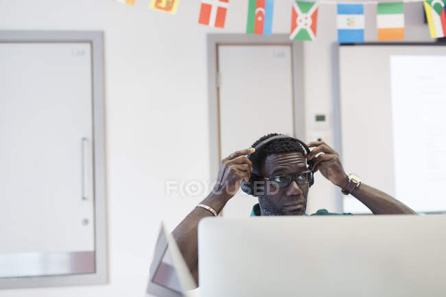 Mature male community college student adjusting headphones at computer in classroom — Stock Photo