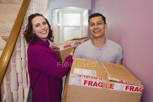Portrait happy couple moving house, carrying cardboard boxes in corridor — Stock Photo