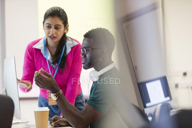 Instrutor universitário comunitário ajudando estudante em computador em sala de aula de laboratório de informática — Fotografia de Stock