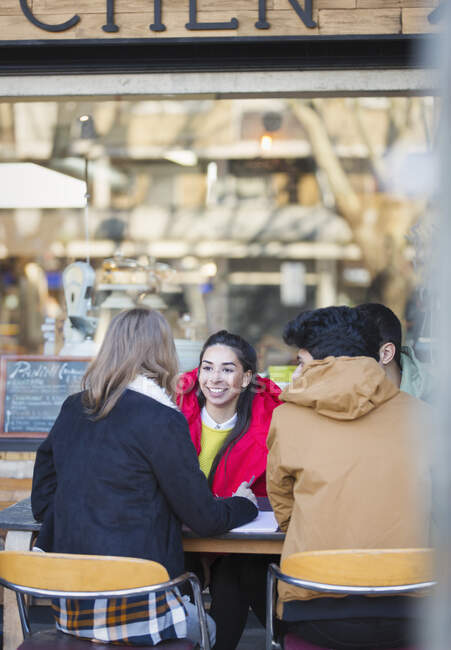 Молодые друзья разговаривают в кафе на тротуаре — стоковое фото