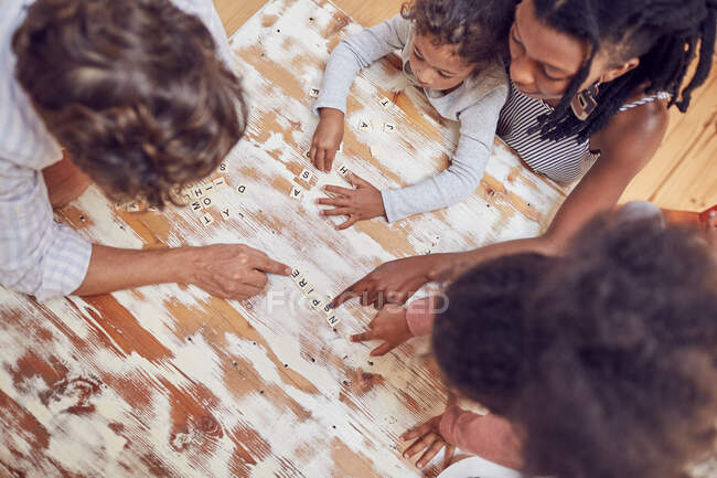 Familia joven jugando scrabble juego de palabras en la mesa - foto de stock