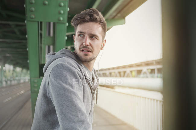 Young male runner with earphones looking over shoulder on train station platform — Stock Photo