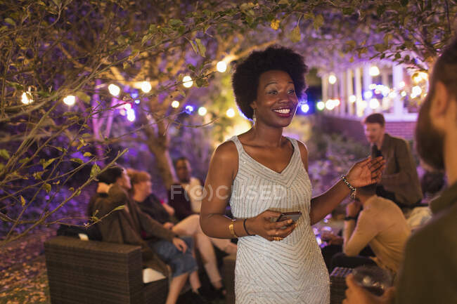 Smiling woman with smart phone talking to friend at garden party — Stock Photo