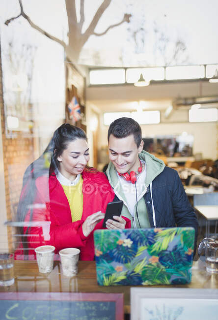 Casal jovem usando telefone inteligente na janela do café — Fotografia de Stock