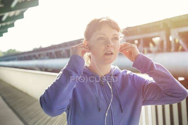 Joven corredora ajustando auriculares, escuchando música - foto de stock