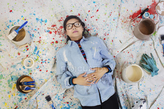 Frau macht Malpause und legt sich auf ein Tuch zwischen Farbdosen — Stockfoto