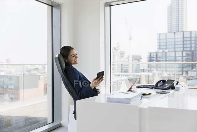 Улыбающаяся деловая женщина с помощью смартфона в городском офисе — стоковое фото