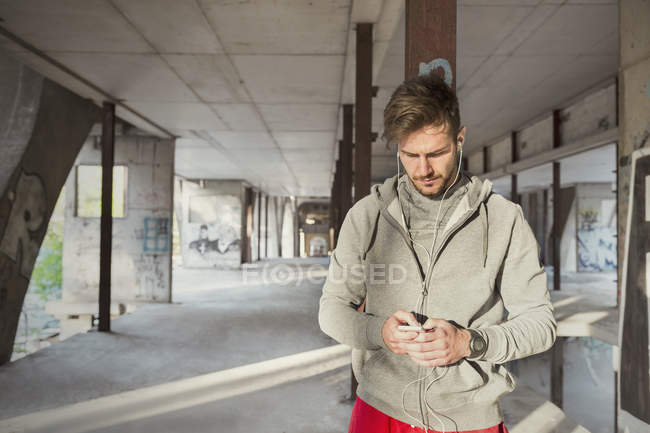 Молодий чоловік бігун слухає музику з mp3 плеєром та навушниками у покинутій будівлі — стокове фото