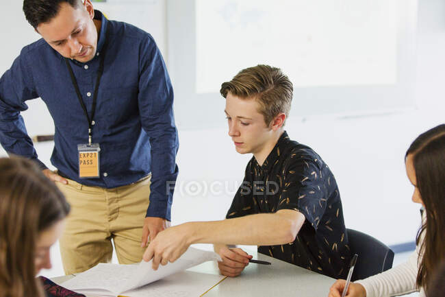 Profesor de escuela secundaria masculino ayudando a estudiante con la tarea en el aula - foto de stock