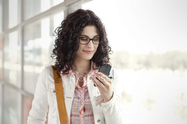 Jovem mulher usando telefone inteligente na janela — Fotografia de Stock