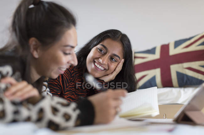Lächelnde Teenager-Freundinnen beim Hausaufgabenmachen im Bett — Stockfoto