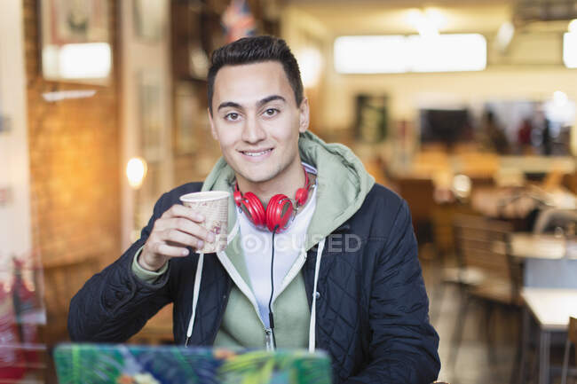 Retrato sonriente, confiado joven estudiante universitario que estudia y bebe café en la ventana de la cafetería - foto de stock