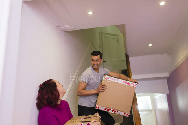 Happy couple moving house, carrying cardboard boxes on stairs — Stock Photo