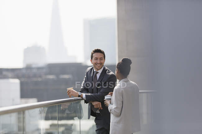 Uomini d'affari che parlano e bevono caffè sul balcone soleggiato e urbano — Foto stock