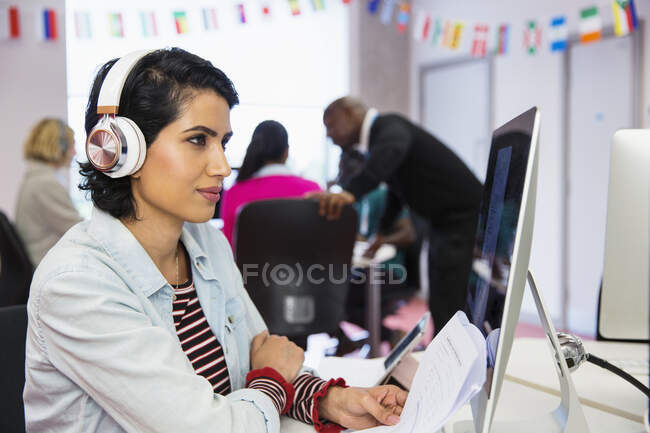 Estudiante universitaria comunitaria enfocada con auriculares usando computadora en el aula - foto de stock