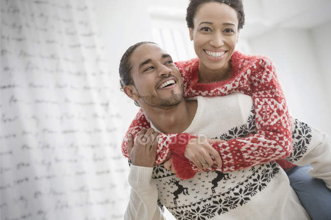 Retrato feliz, pareja juguetona en suéteres de Navidad piggybacking - foto de stock