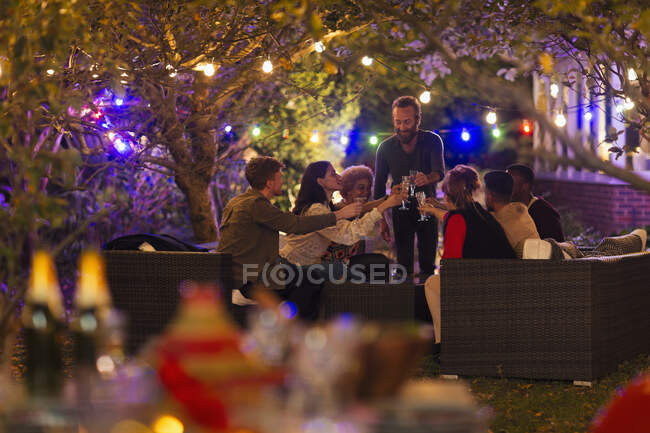 Amigos bebendo debaixo de árvores com luzes de corda na festa do jardim — Fotografia de Stock