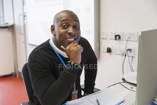 Retrato confidente instructor de universidad comunitaria masculina en la computadora en el aula - foto de stock