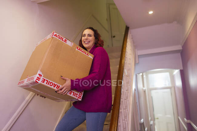 Portrait smiling woman moving house, carrying cardboard box on stairs — Stock Photo
