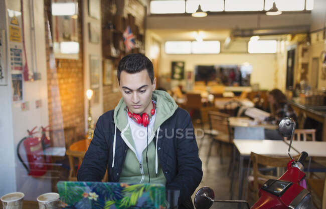 Enfocado joven estudiante universitario que estudia en el portátil en la ventana de la cafetería - foto de stock