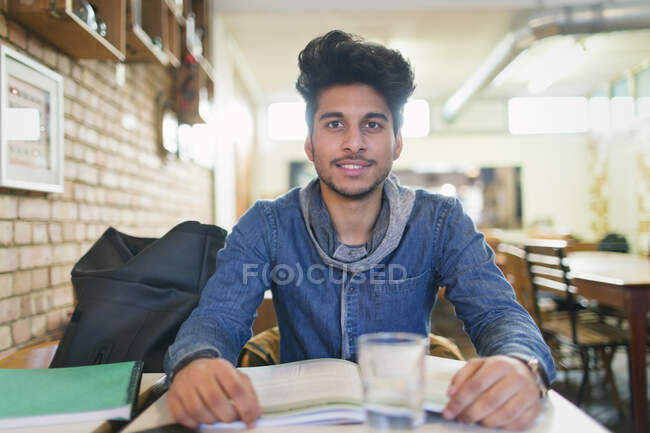 Retrato confiado joven estudiante universitario que estudia en la cafetería - foto de stock