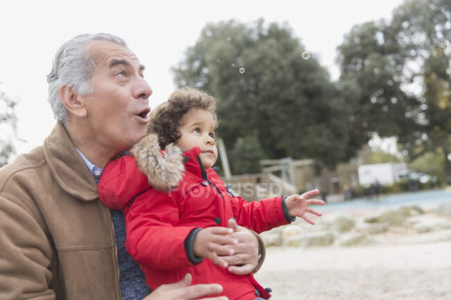 Дедушка и внук играют с пузырьками в парке — стоковое фото