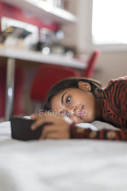 Дівчина-підліток за допомогою смартфона, який грає на ліжку — стокове фото