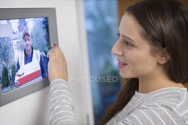 Женщина наблюдает за курьером на входной двери от монитора системы безопасности дома — стоковое фото
