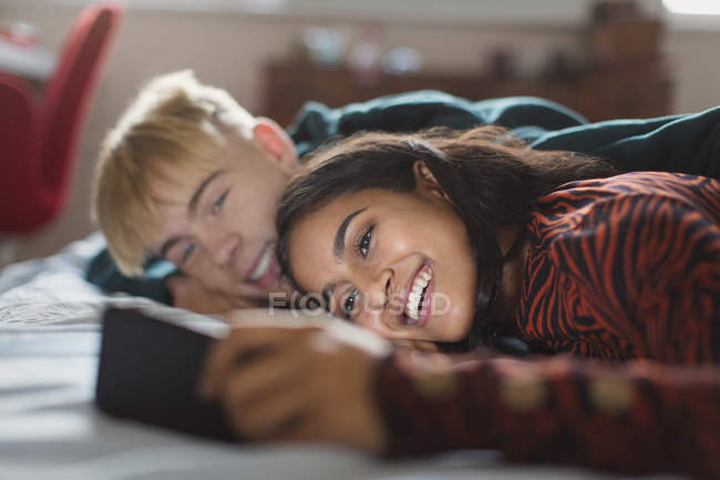 Teenage couple using smartphone, laying on bed — Stock Photo