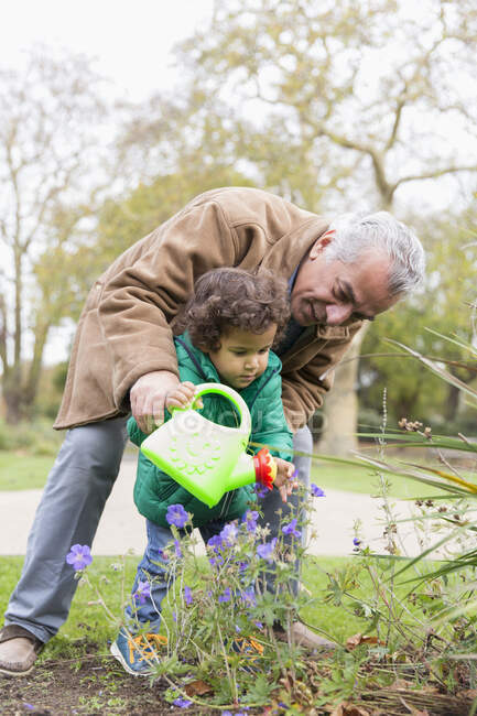 Grandfather and granddaughter watering flowers with watering can — Stock Photo